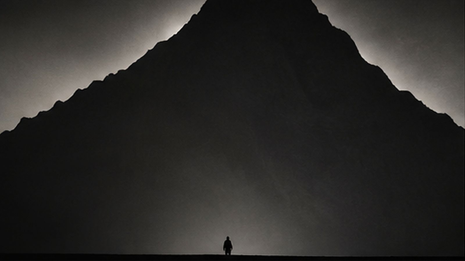 A lone figure at the foot of an enormous mountain