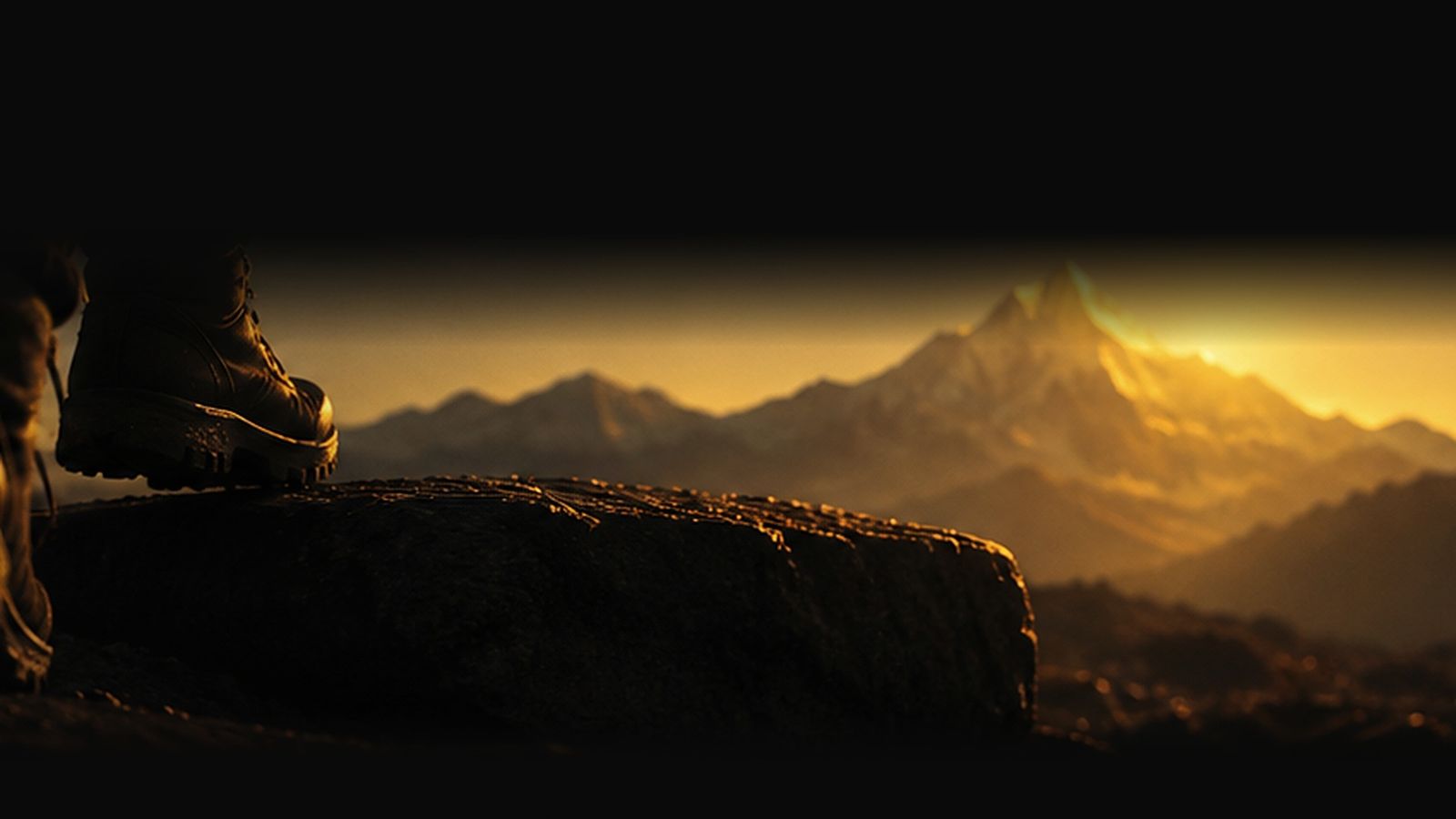 A hiking boot on a rock, a mountain at dawn behind it